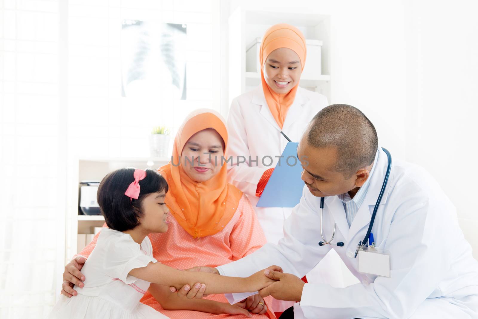 Southeast Asian child patient consulting medical doctor. Muslim family. Little girl with broken arm doing health check.