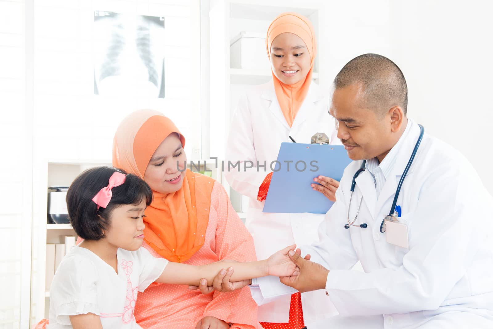 Southeast Asian kid patient consulting medical doctor. Muslim family. Little girl with broken arm doing checkup.