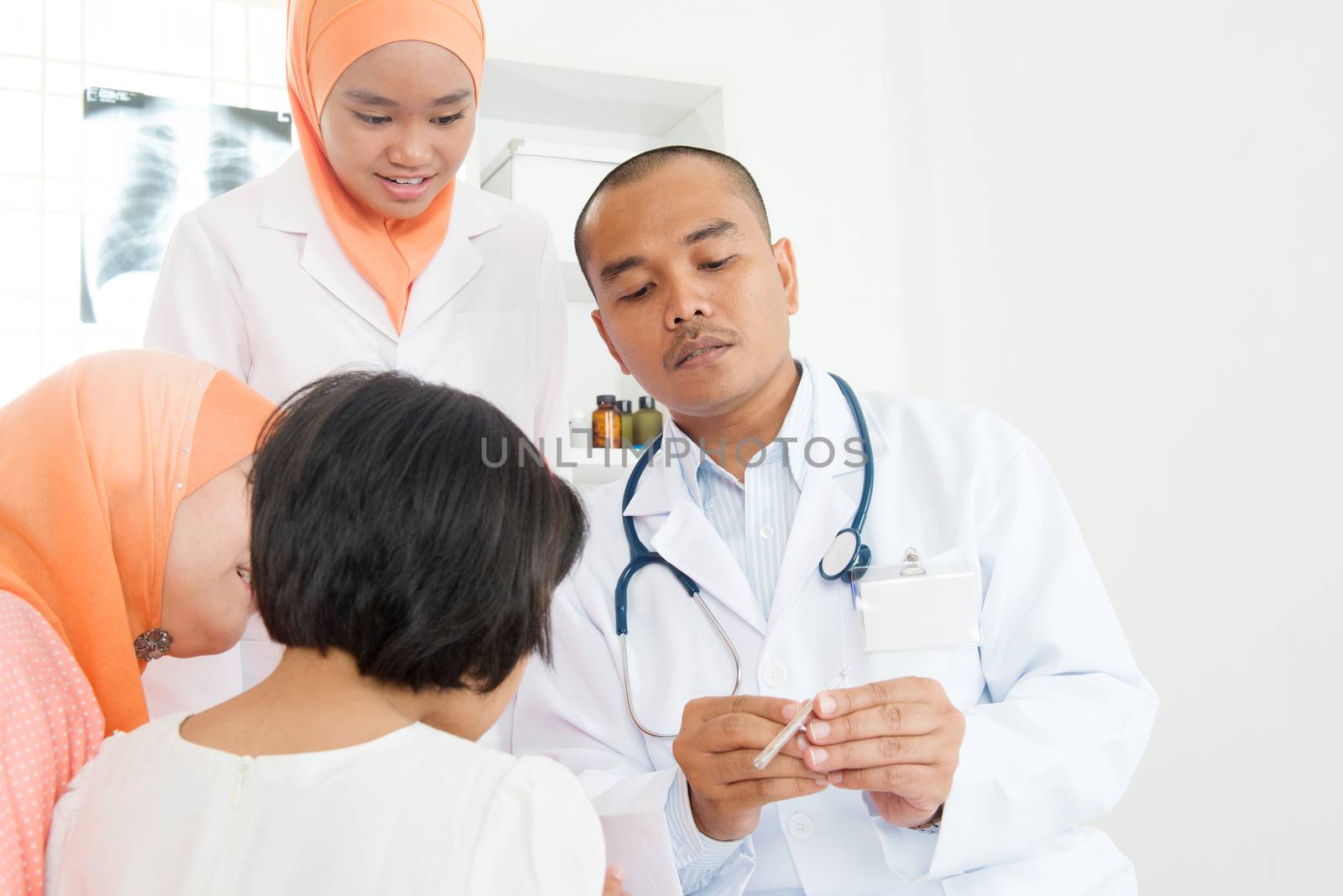 Doctor checking little girl's temperature at hospital.  Southeast Asian Muslim family.