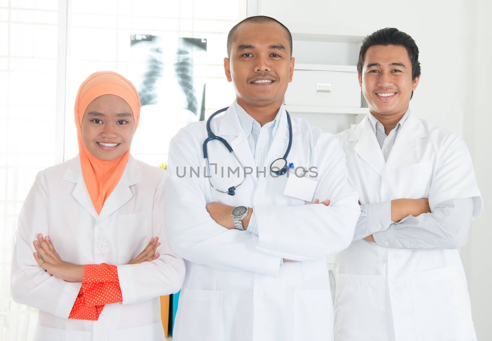 Medical team crossed arms standing inside hospital. Southeast Asian Muslim doctors and nurses.