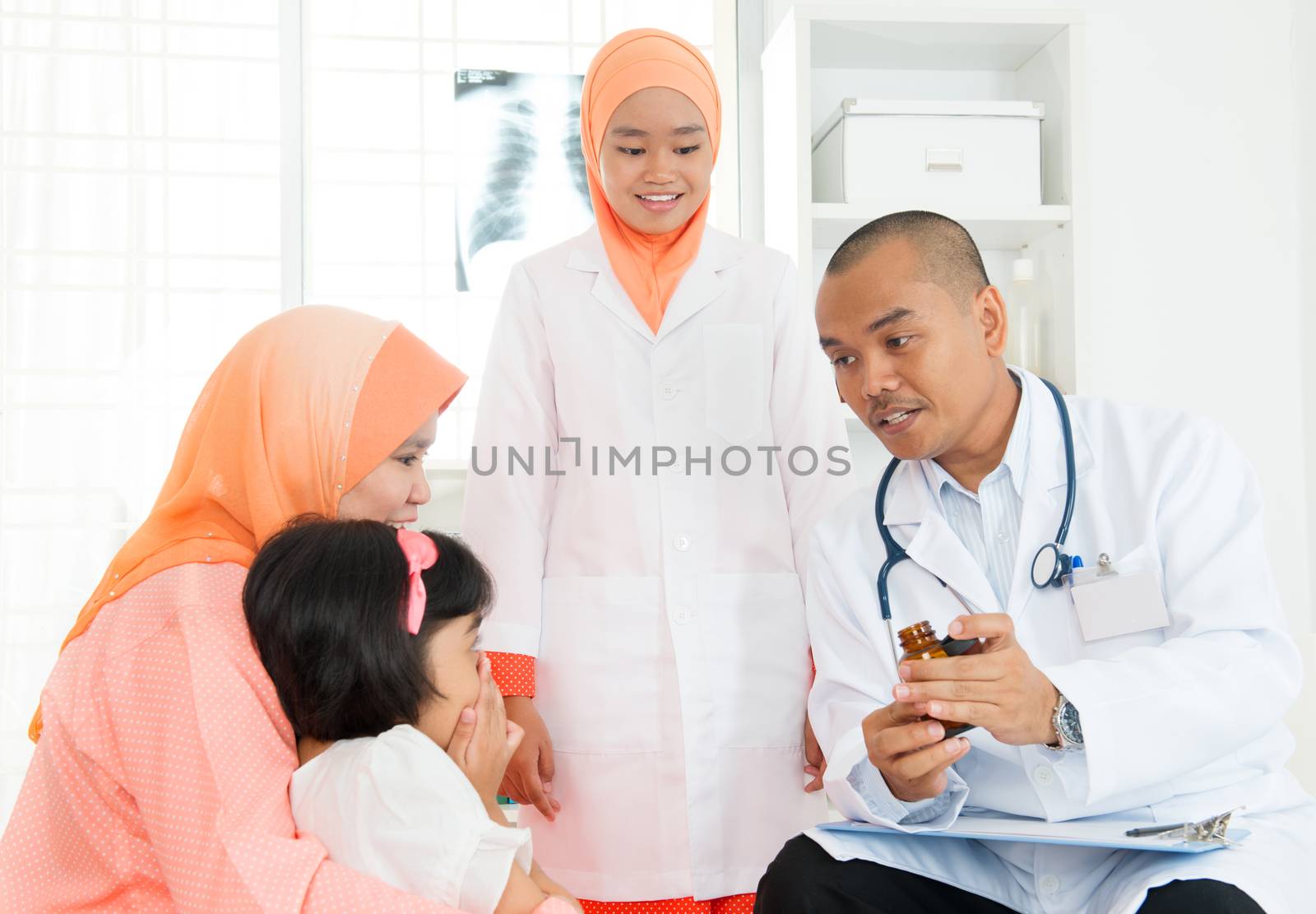 Asian male doctor explaining medicine usage to little patient's parent. Family medical concept.