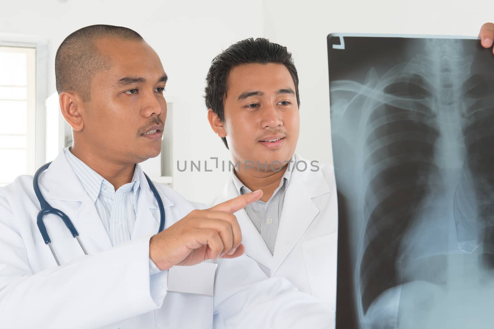 Medical doctors checking on x-ray image standing inside hospital room. Southeast Asian Muslim people.
