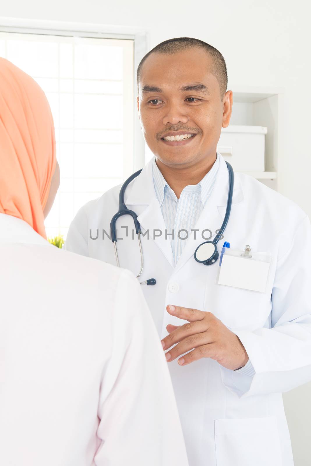 Medical doctor talking with nurse inside hospital. Southeast Asian Muslim people.