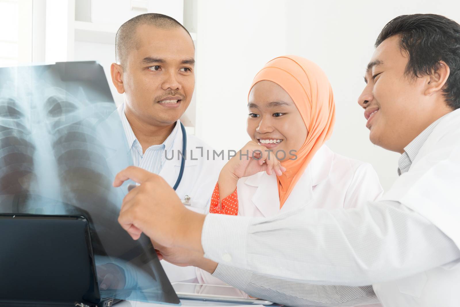 Surgeon and doctor analyzing x-ray together in medical office. Southeast Asian Muslim people.