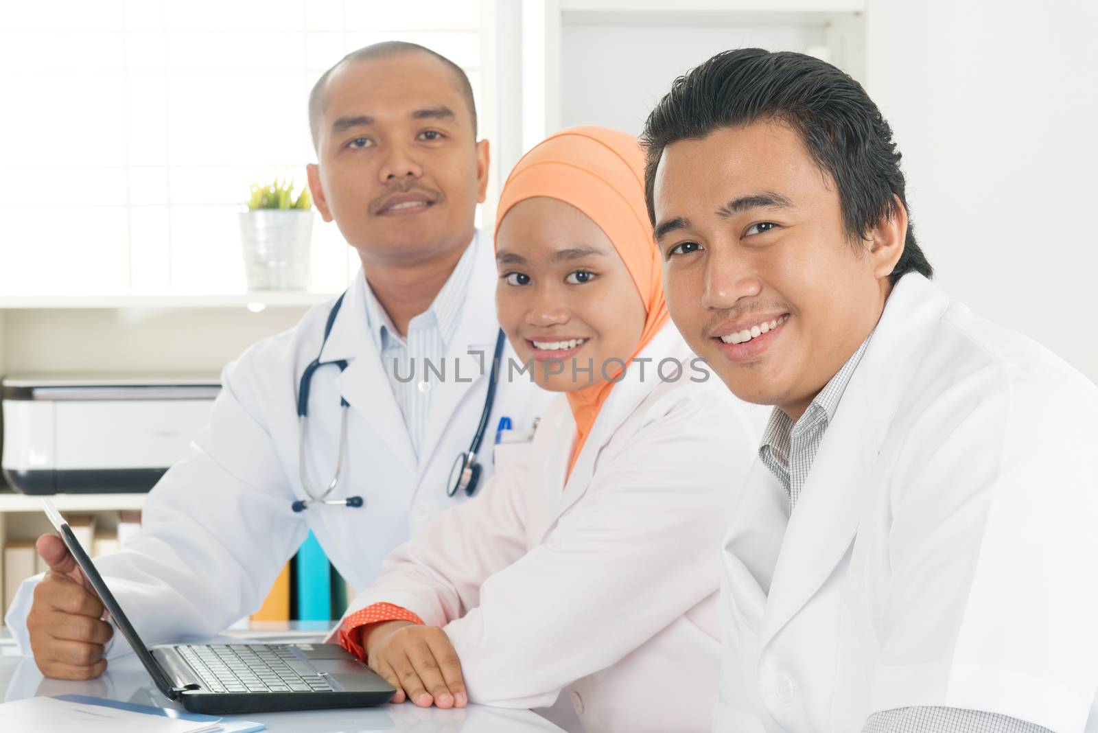 Medical team discuss at meeting in hospital office. Southeast Asian Muslim doctors and nurses.