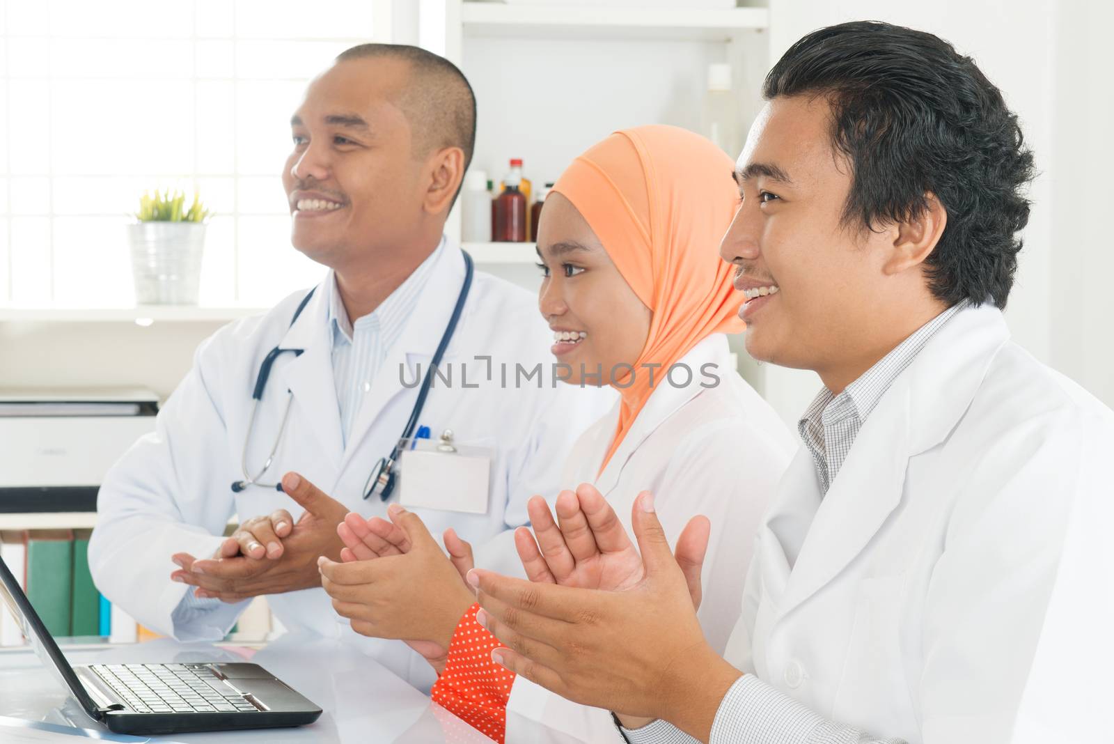Joyful medical team clapping hands during a meeting, Southeast Asian Muslim doctors and nurses.