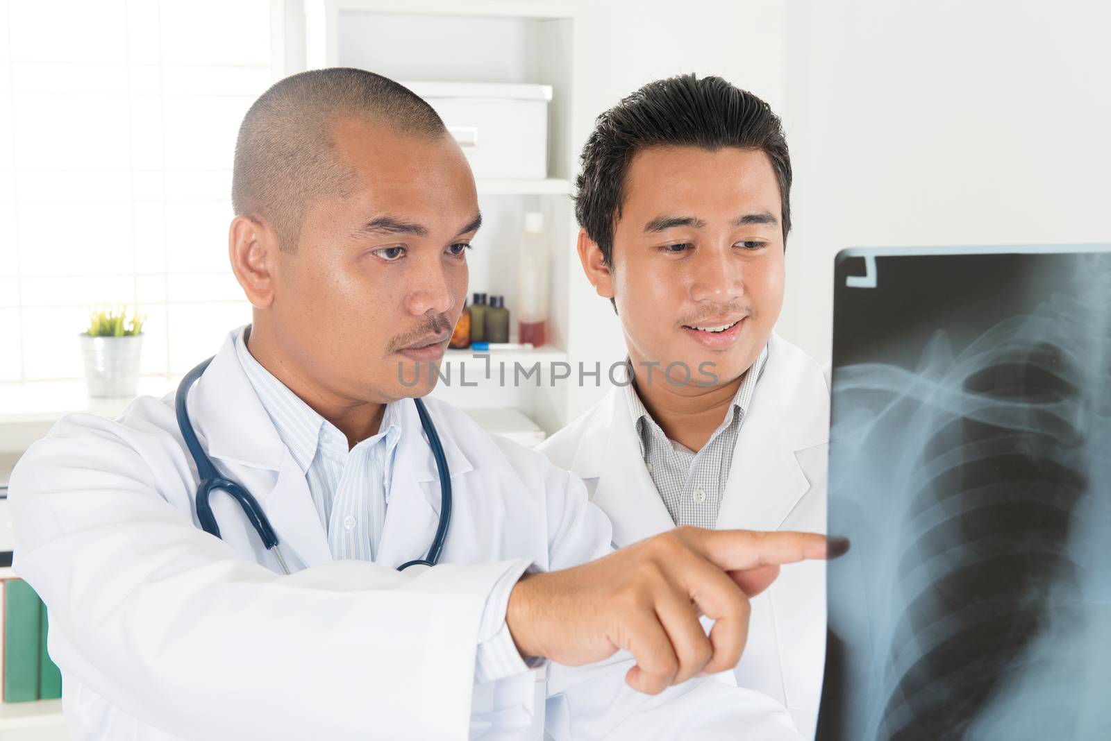 Doctors analyzing x-ray together in medical office. Southeast Asian Muslim people.