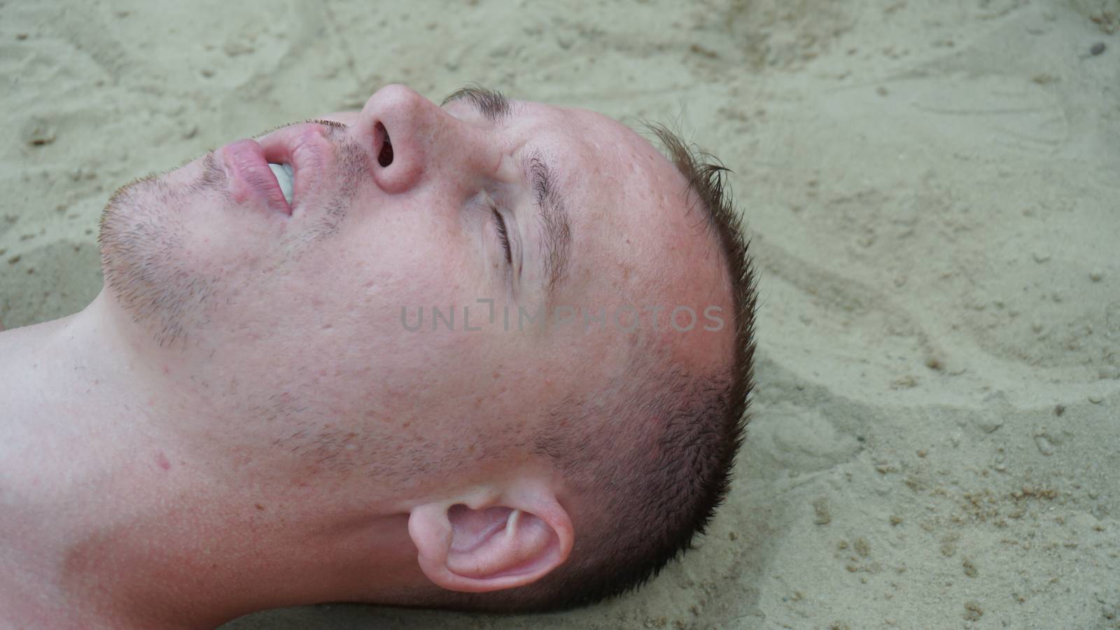 a young man lies on the sand on the beach by nolimit046