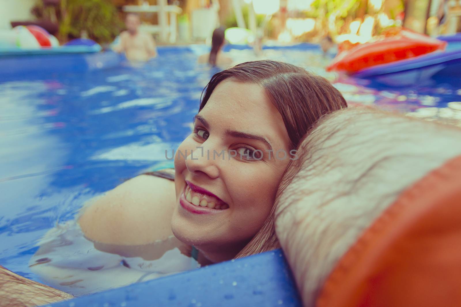 Beautiful smiling woman lays her head on the leg of a man in a swimming pool.