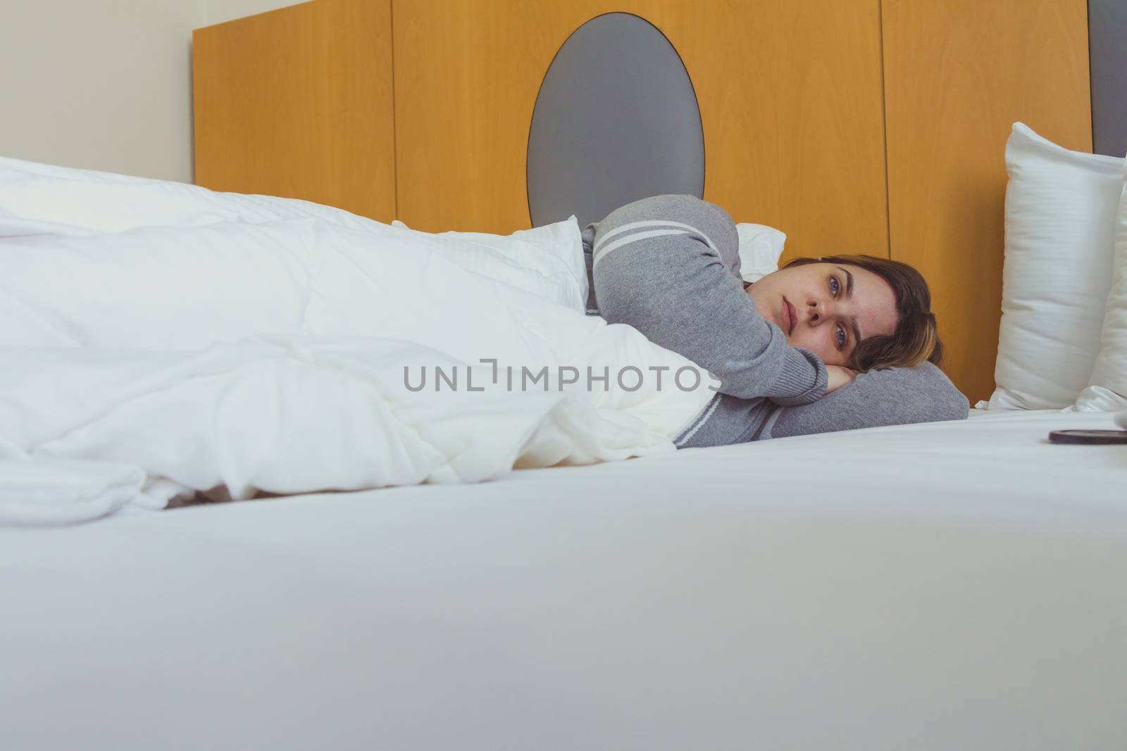 Young woman daydreaming while lying on bed under the blanket.