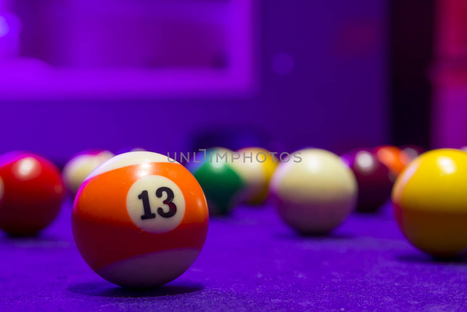 Billiard balls in a pool table. focus on the orange number 13 ball.