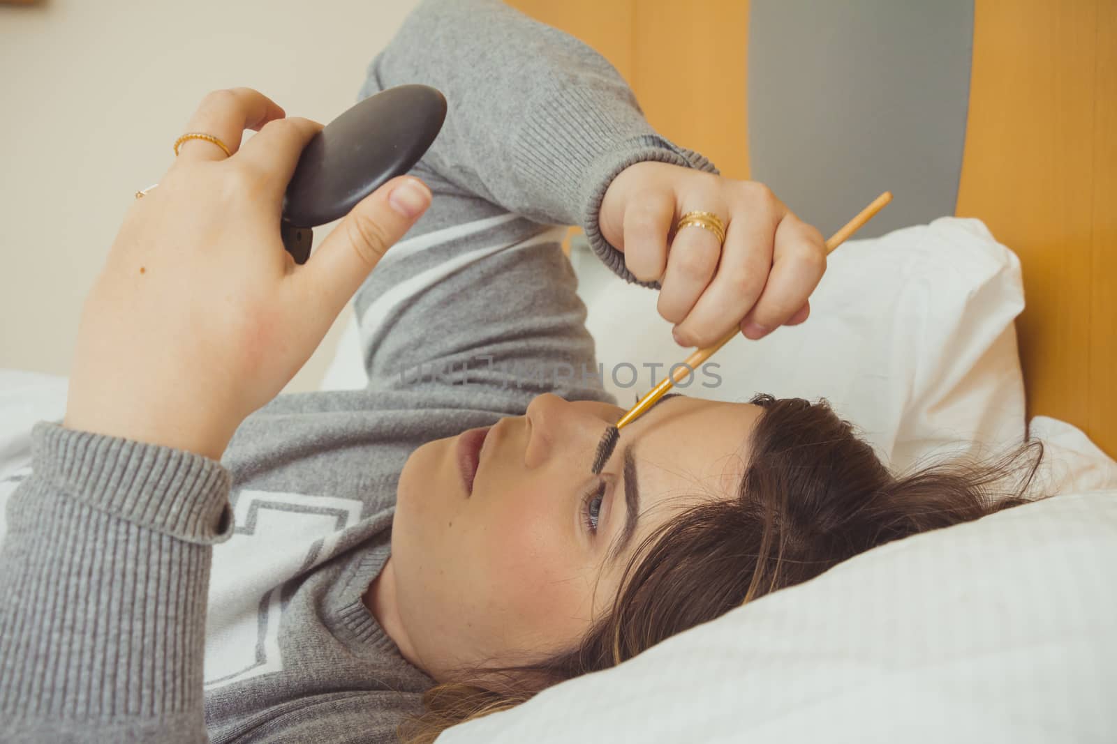 Woman applying makeup while she is lying on her bed