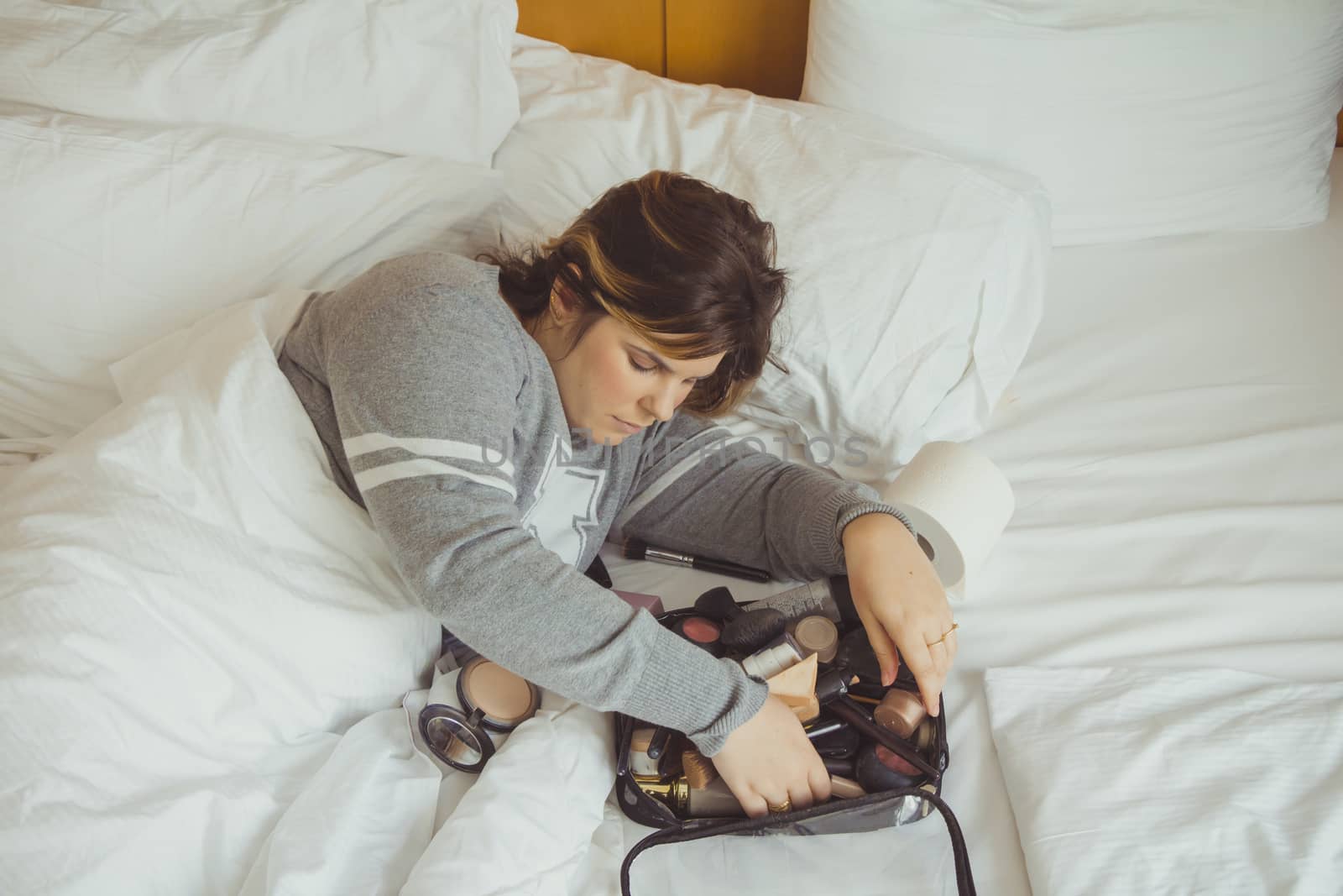 Woman applying makeup while she is lying on her bed.