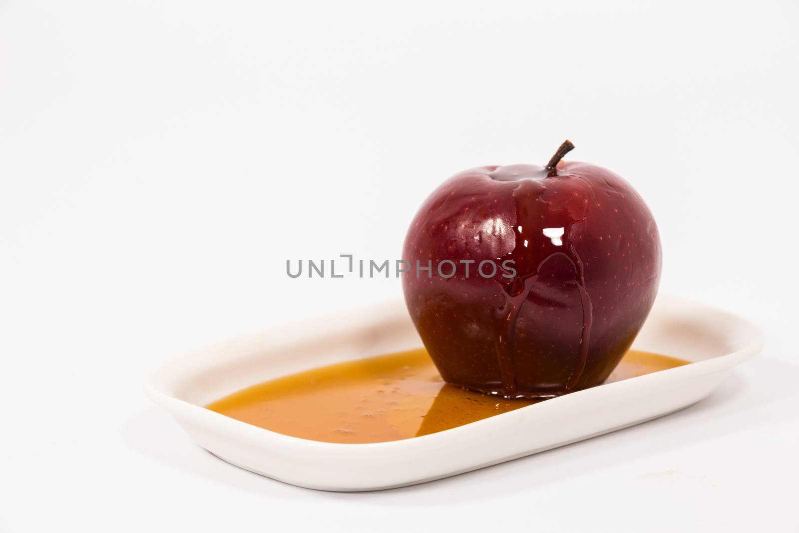 Red apple with drops of honey on white plate with honey isolated on a white background. Symbols of Jewish New Year - Rosh Hashanah.  
