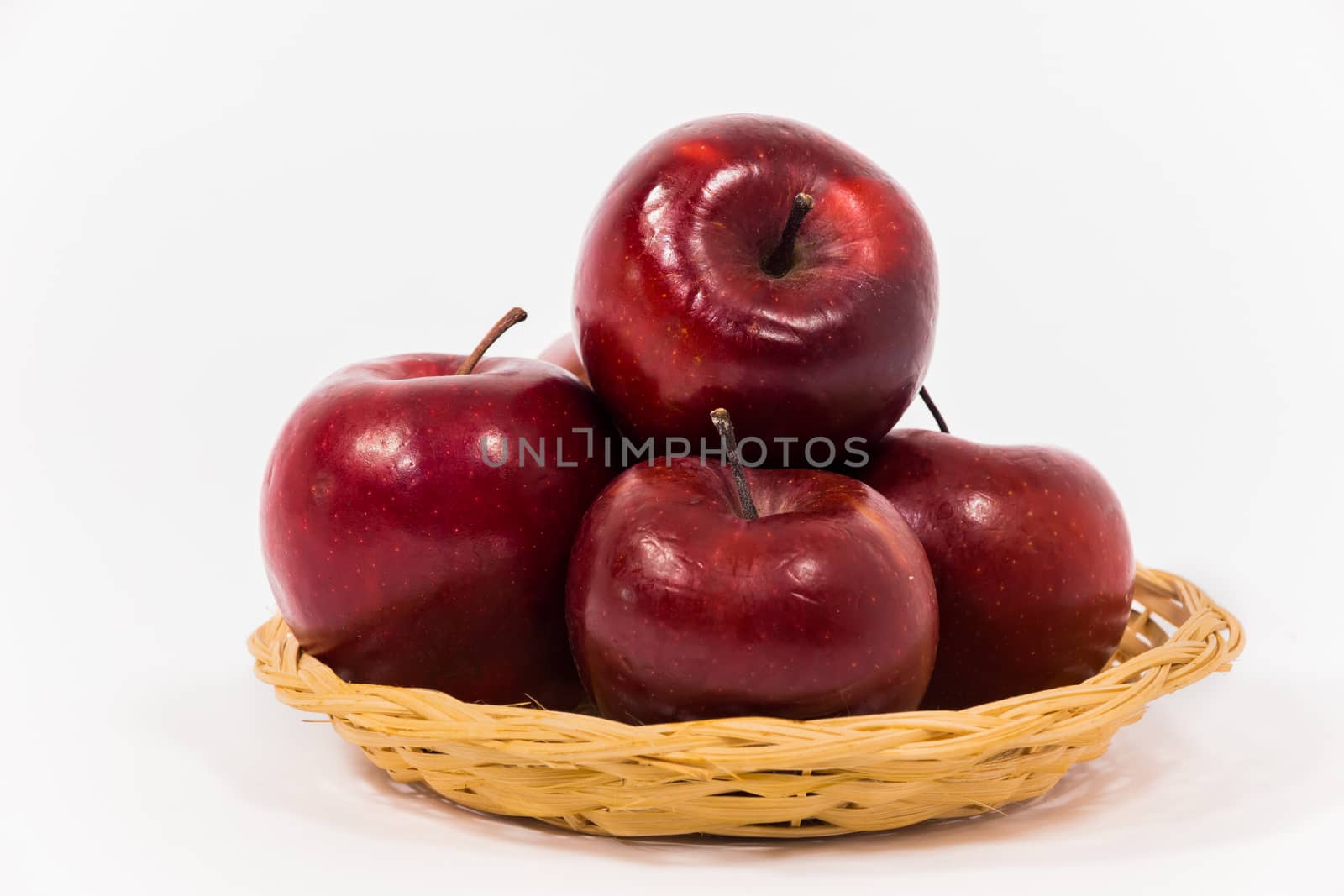 Close up of ripe red apples in wicker basket isolated on white background.