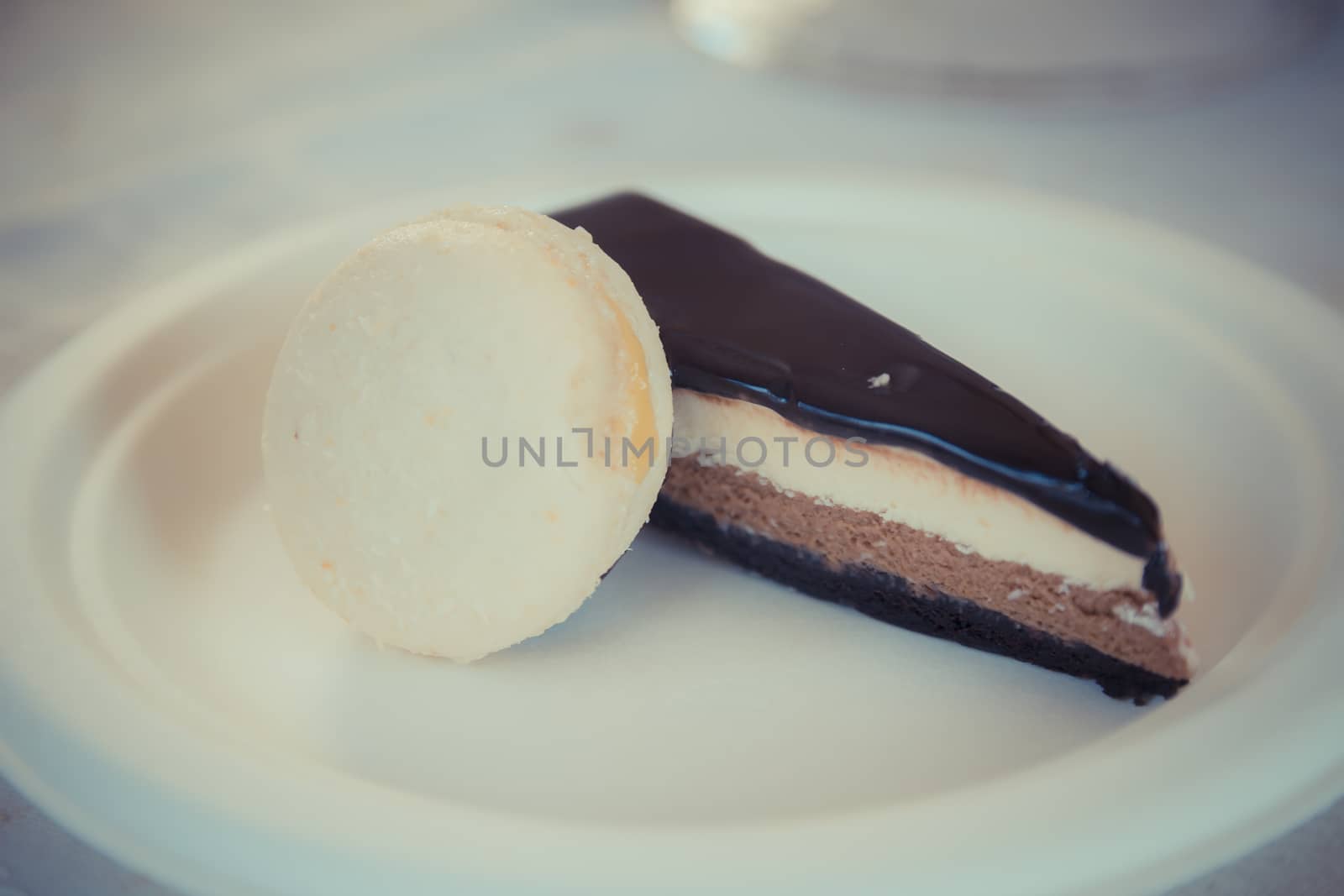 Piece of chocolate-vanilla mousse cake with Glsaz of chocolate and white macaroon on a white plate. 
