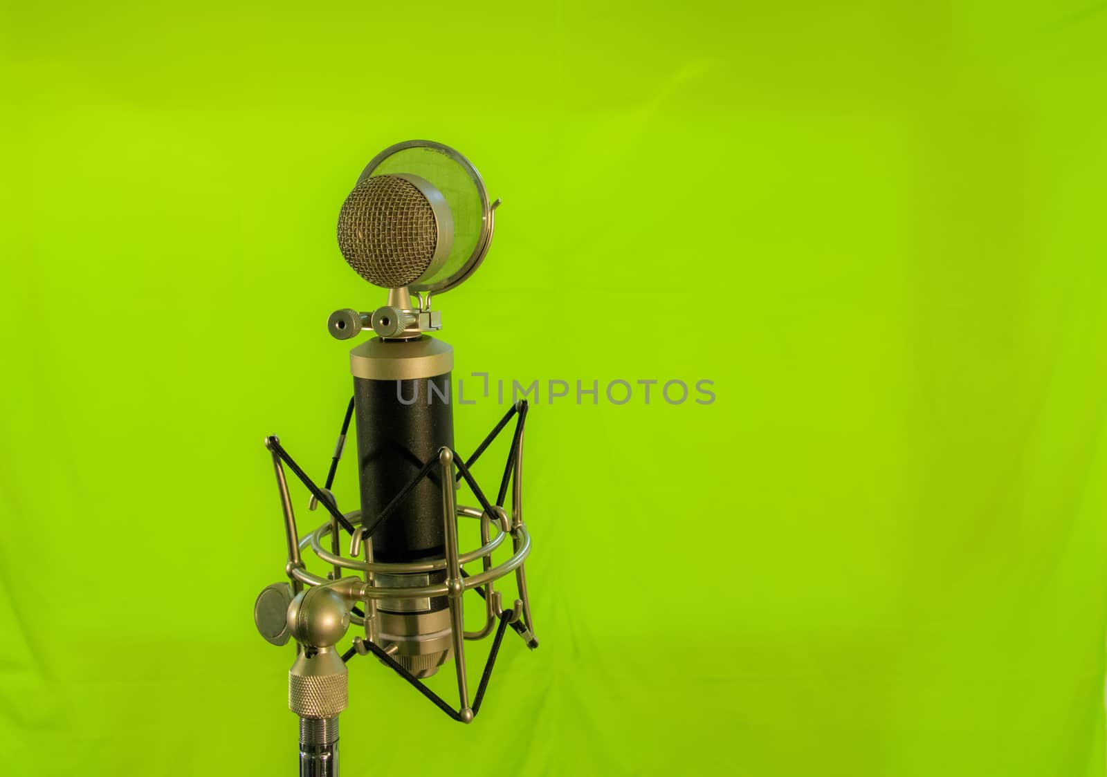 Vocal condenser microphone with wind screen isolated on green background.