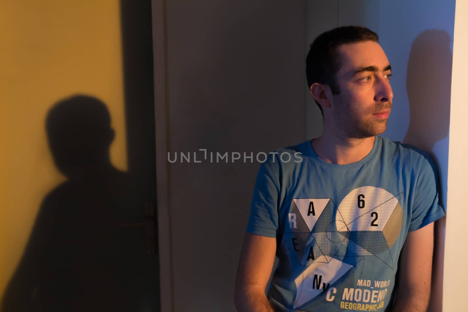 Caucasian man leaning against the wall and looking away when he is in deep thought. He is in a room during sunset at the afternoon.
