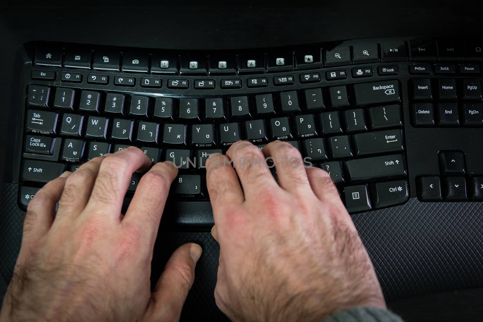 Man typing on a keyboard with letters in Hebrew and English - Wireless keyboard - Top View - Dark atmosphere