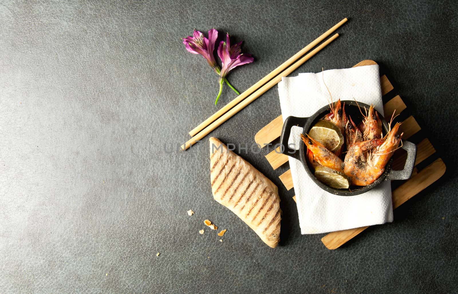 Cooked king prawns in a cast iron pan with chopsticks and bread 