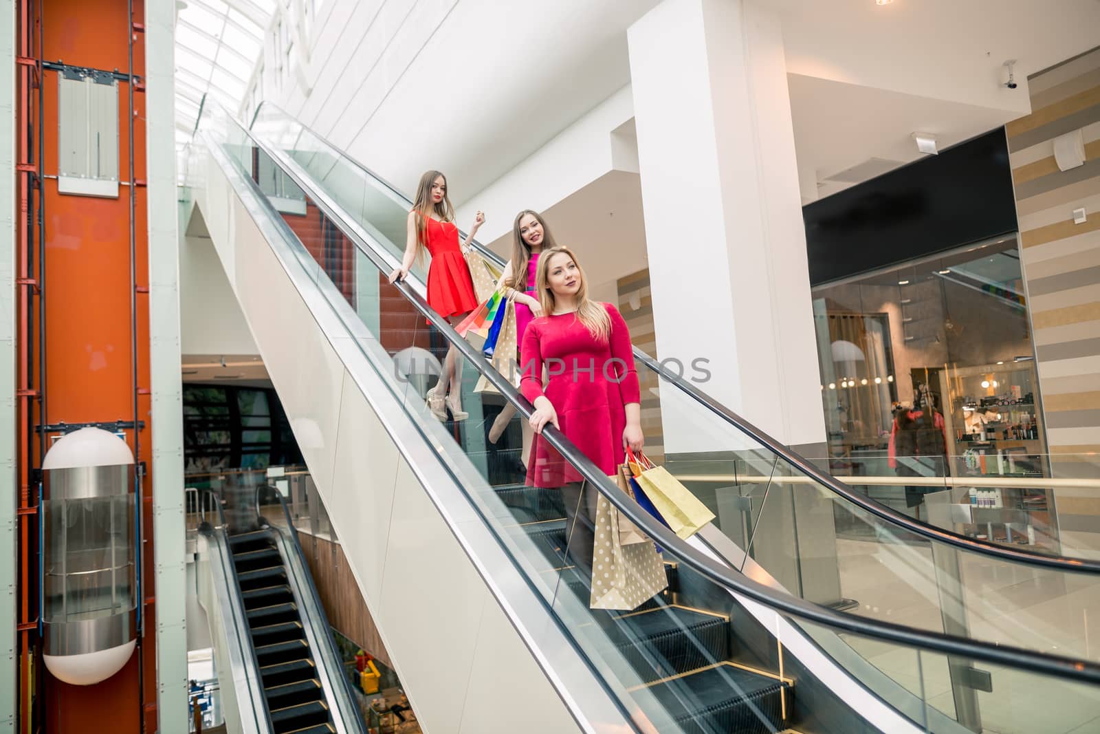 three girlfriends on escalator with shopping bags