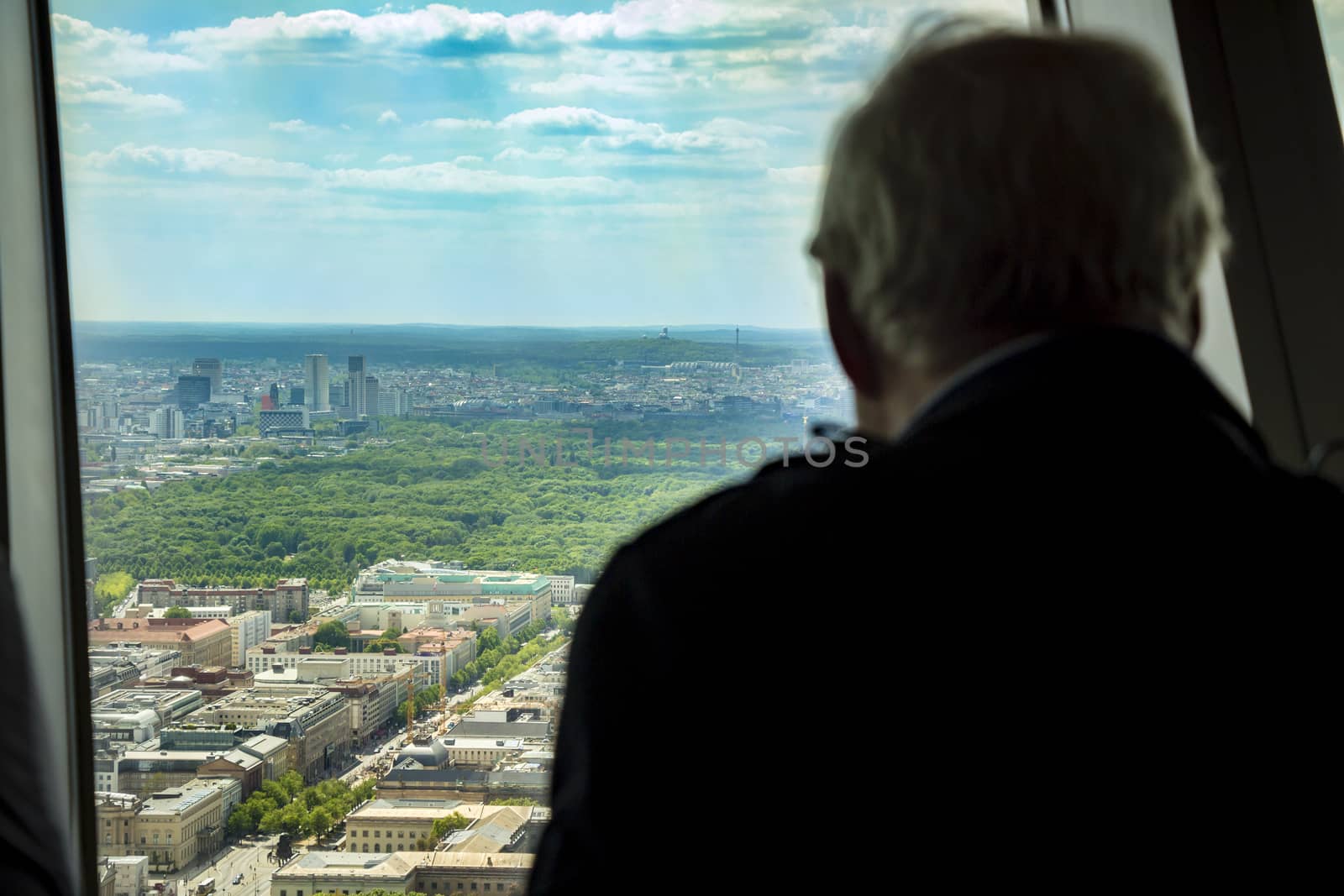 Silhouette of back view of man looking out of a window at the berlin city skyline.