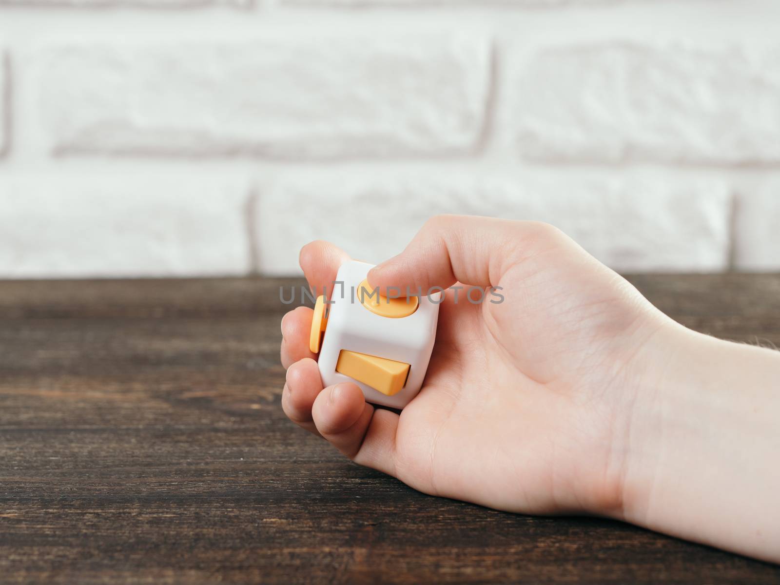 Fidget cube stress reliever in hand over brown wooden background. Fingers antistress toy in hand with copy space.