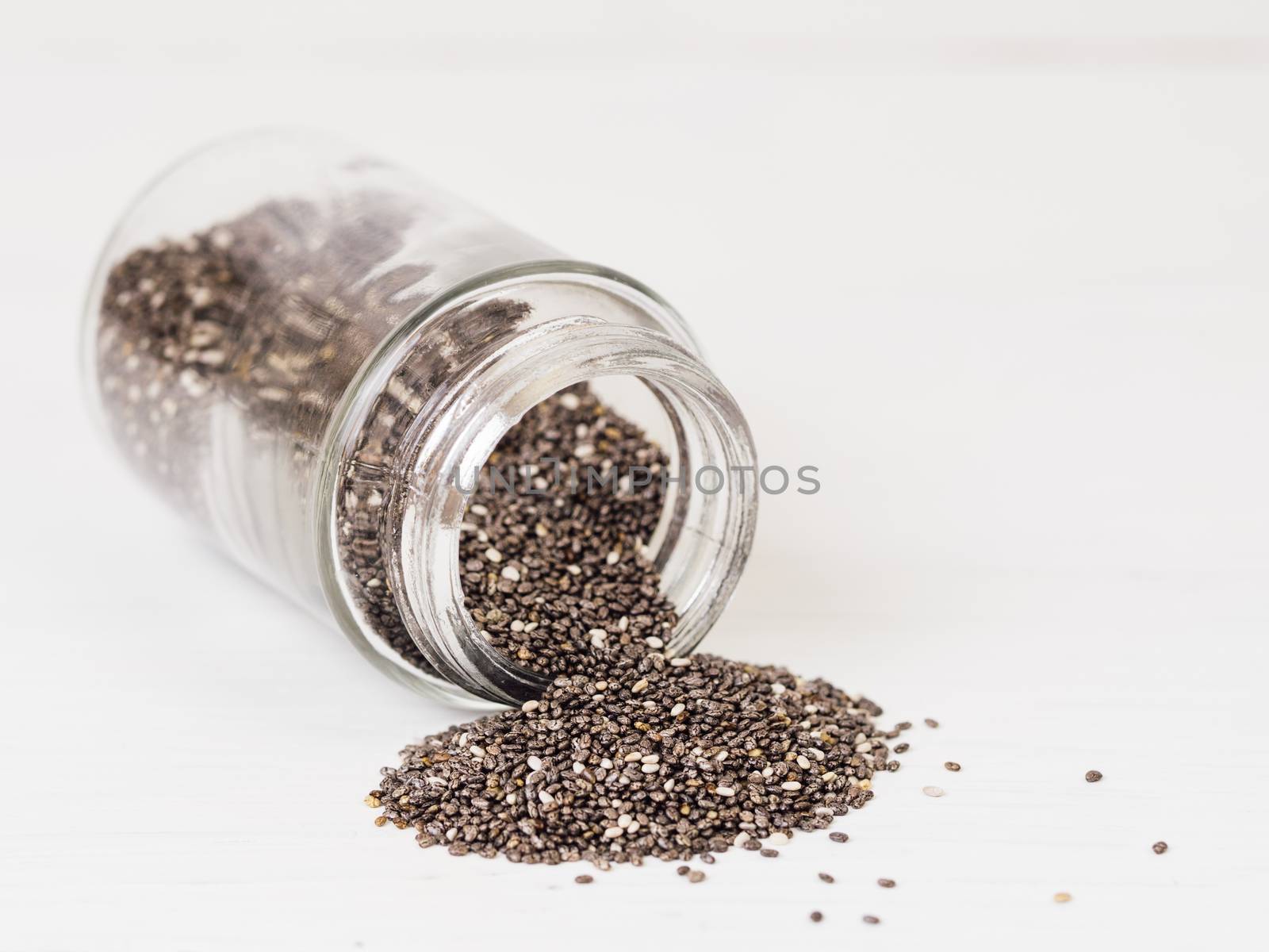 chia seeds scattered from glass jar on white background. Copy space.