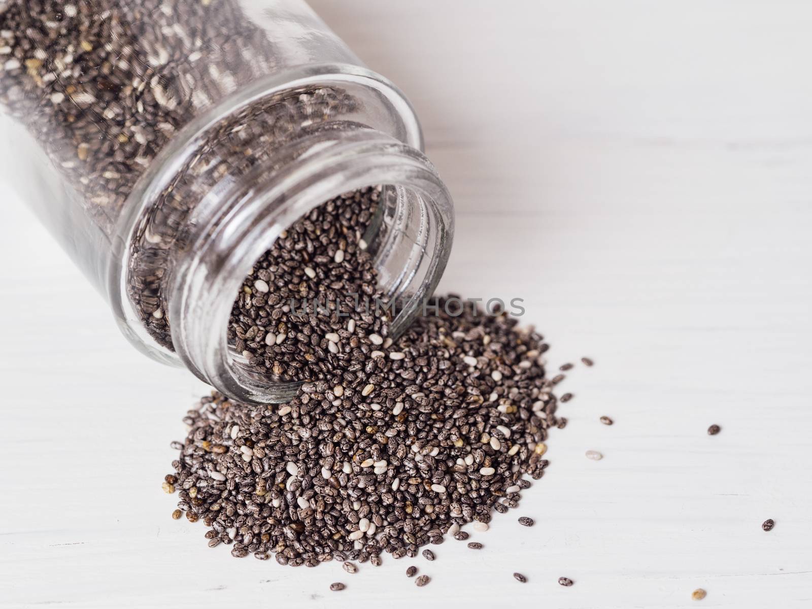 chia seeds scattered from glass jar on white background. Copy space.