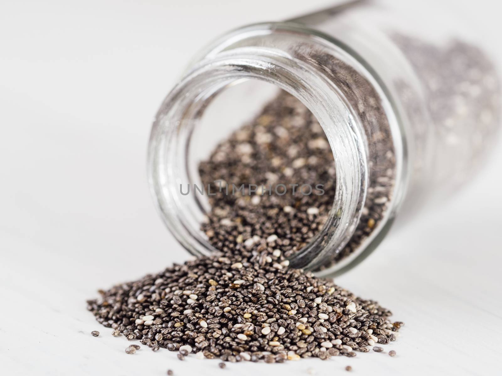 chia seeds scattered from glass jar on white background. Copy space.