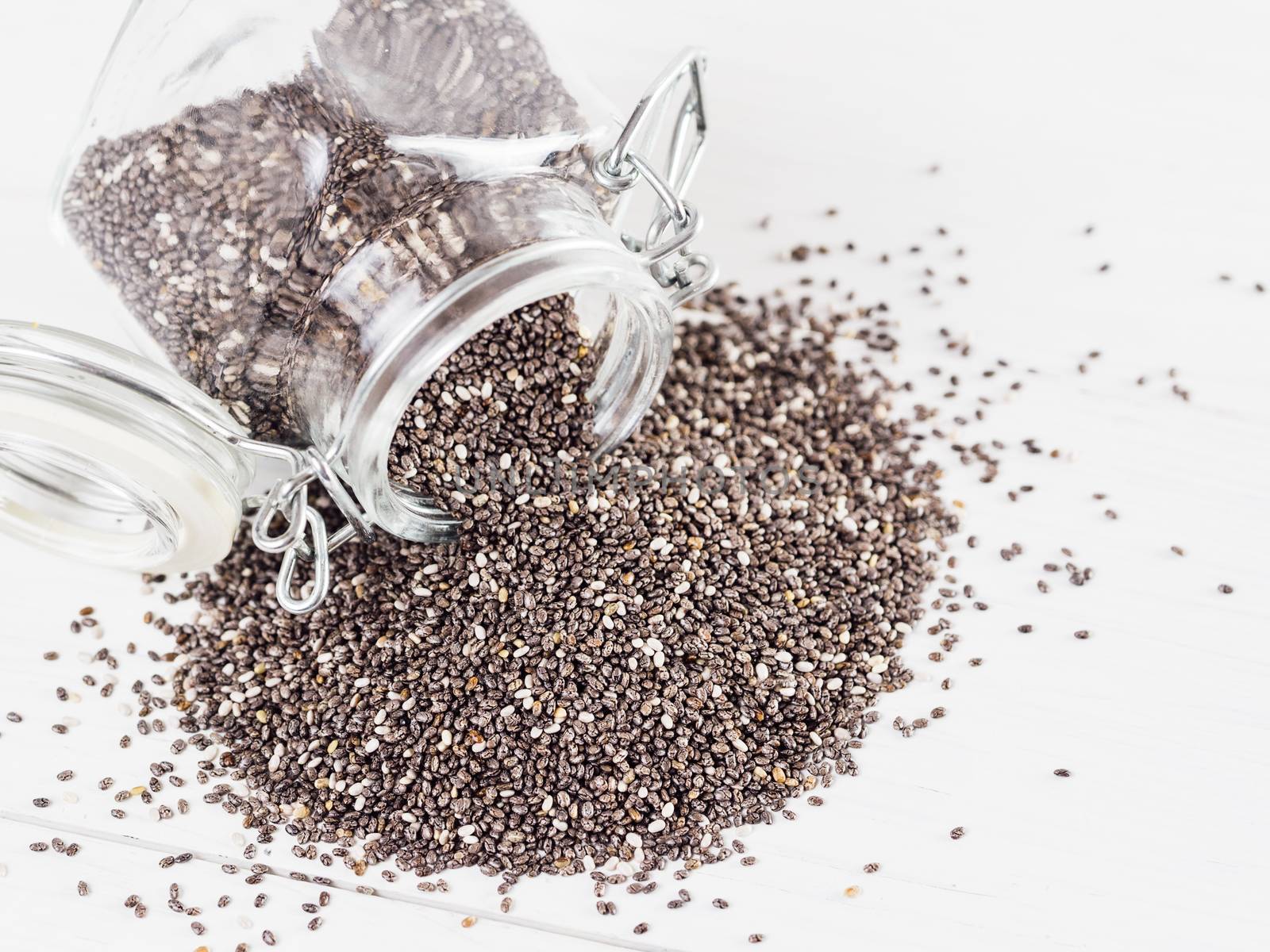 chia seeds scattered from glass jar on white background. Copy space.