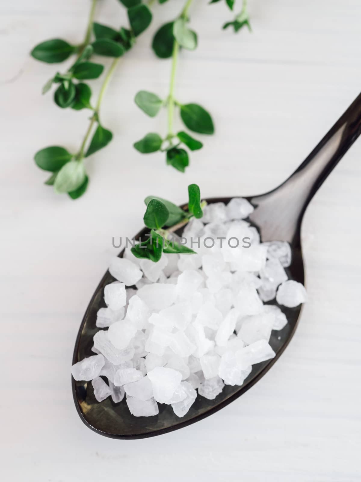 coarse sea salt in black spoon on white background with thyme. Copy space. Top view or flat lay.