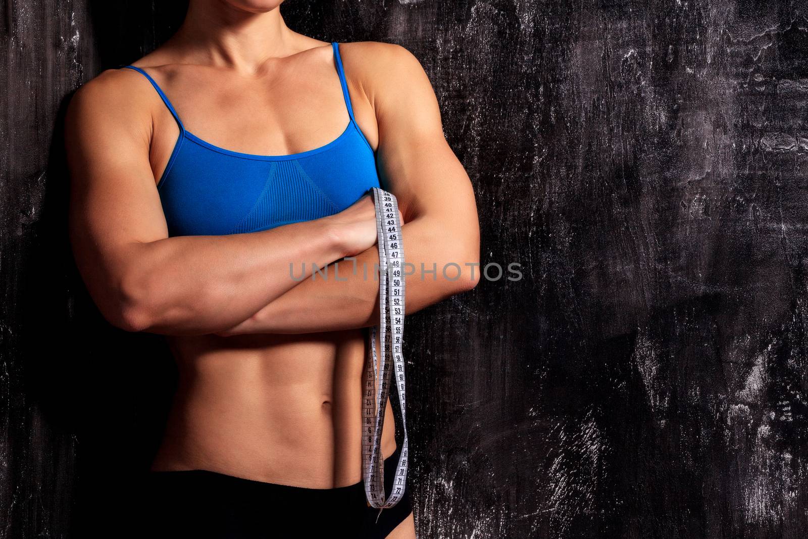 Strong fitness woman with a tape measure on dark background by Nobilior