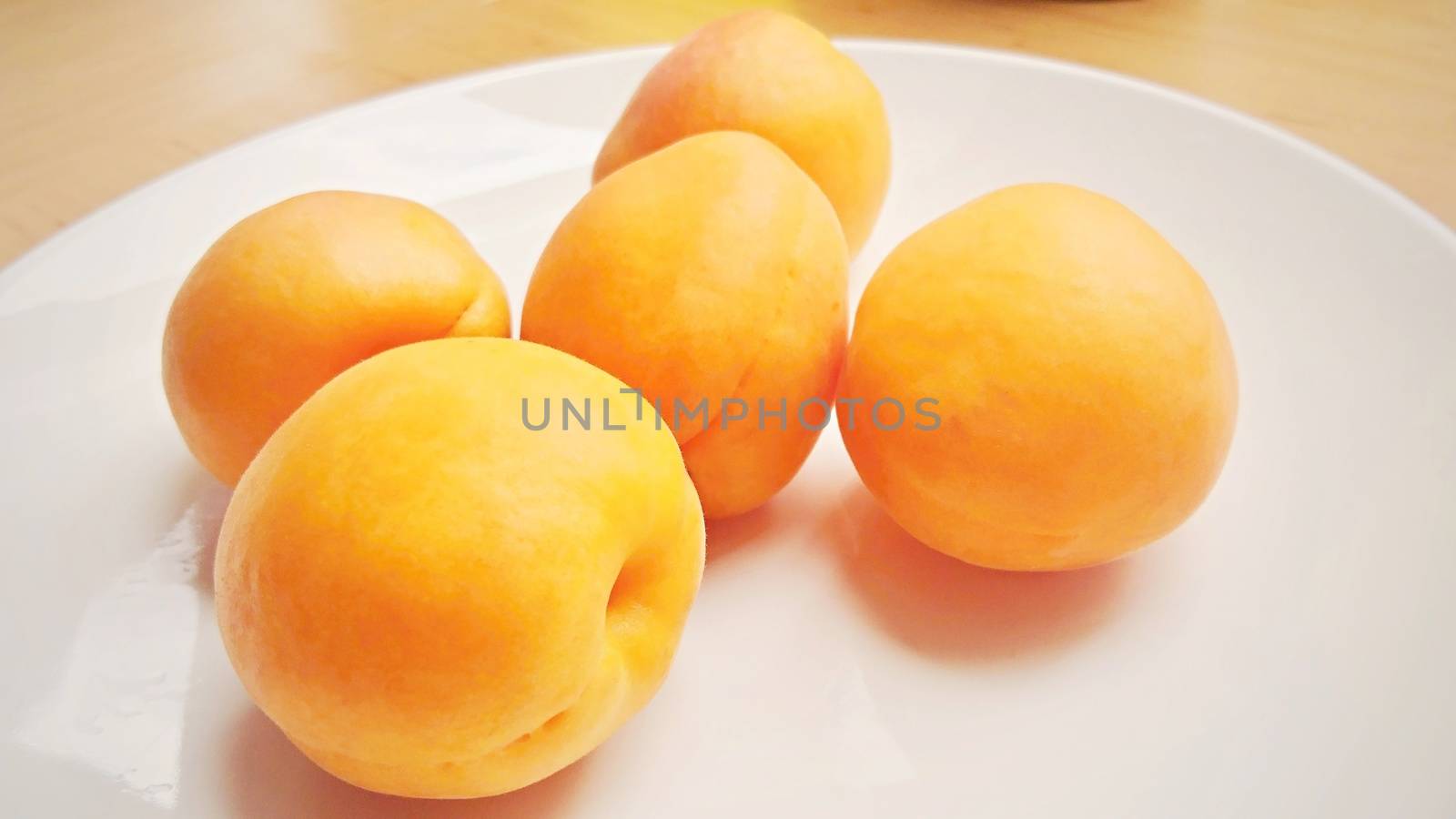 Group of five apricots on a white plate.