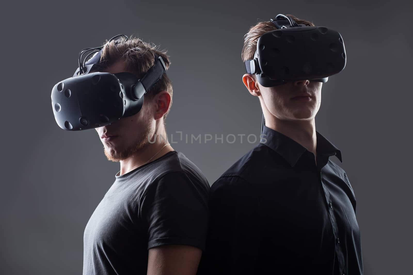 Shot of two young man standing back to back with VR goggles