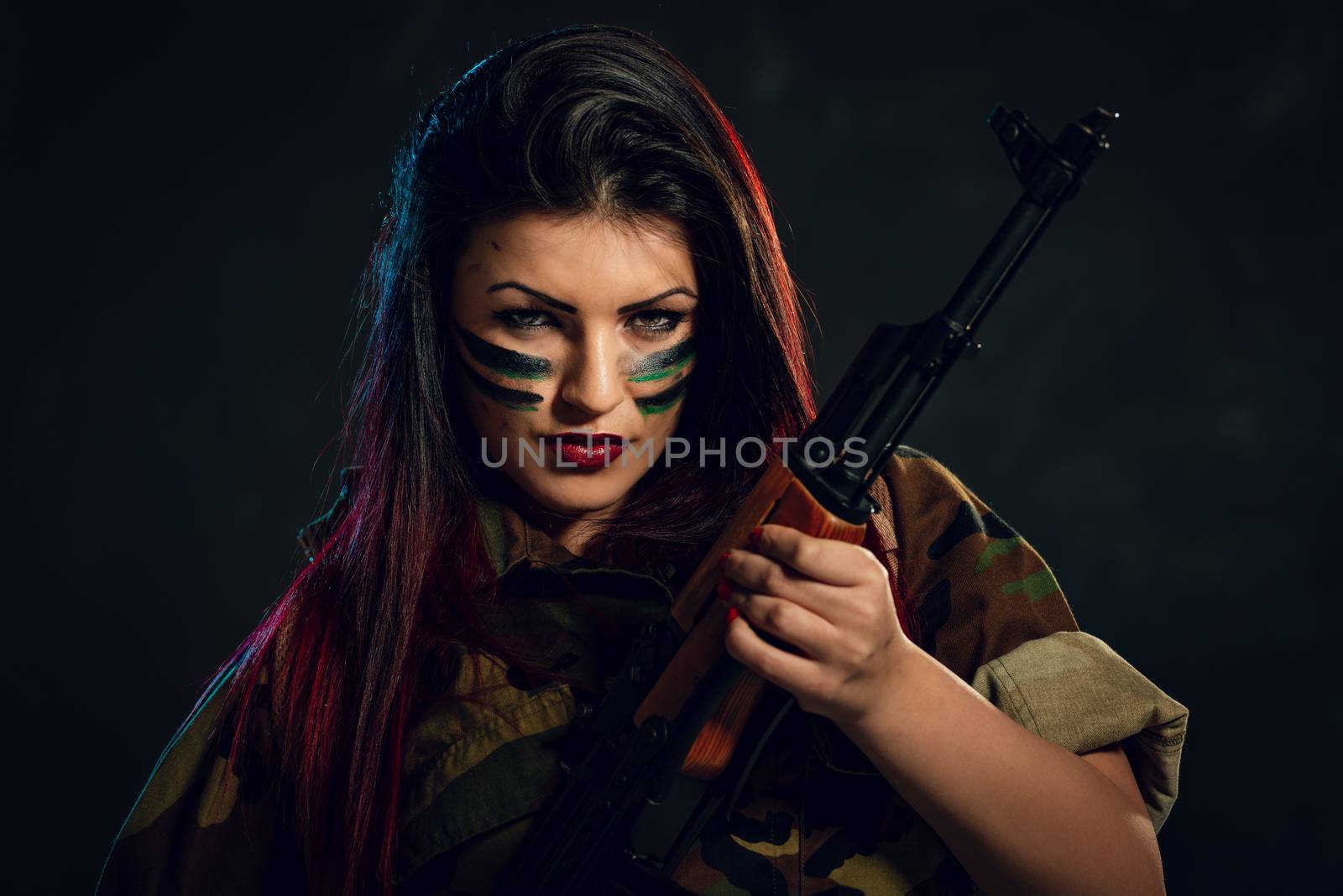Young attractive military woman with face paint in war paint holding rifle and looking at camera.
