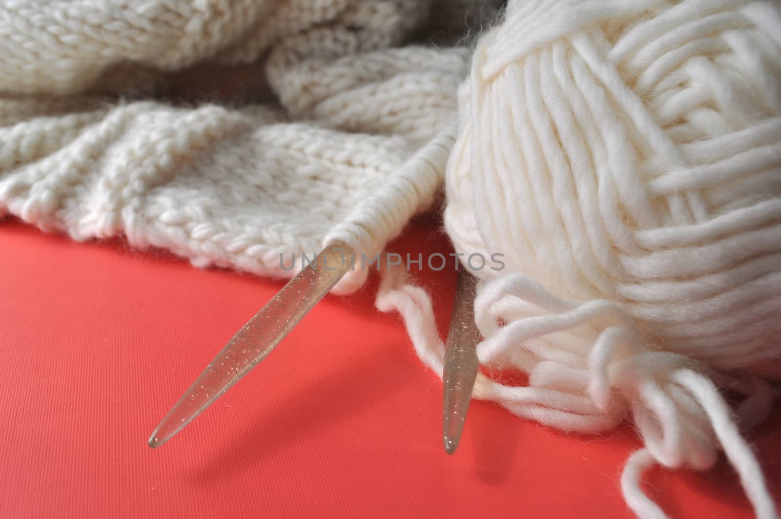 White wool knitting needles and handmade knits on bright orange
