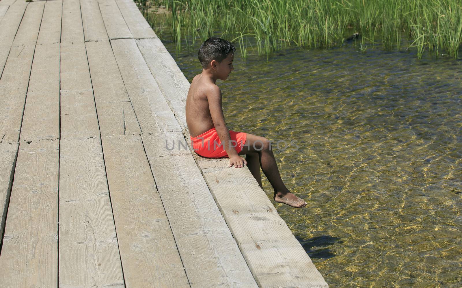 Boy seating on a wooden foot bridge on a lake by nachrc2001