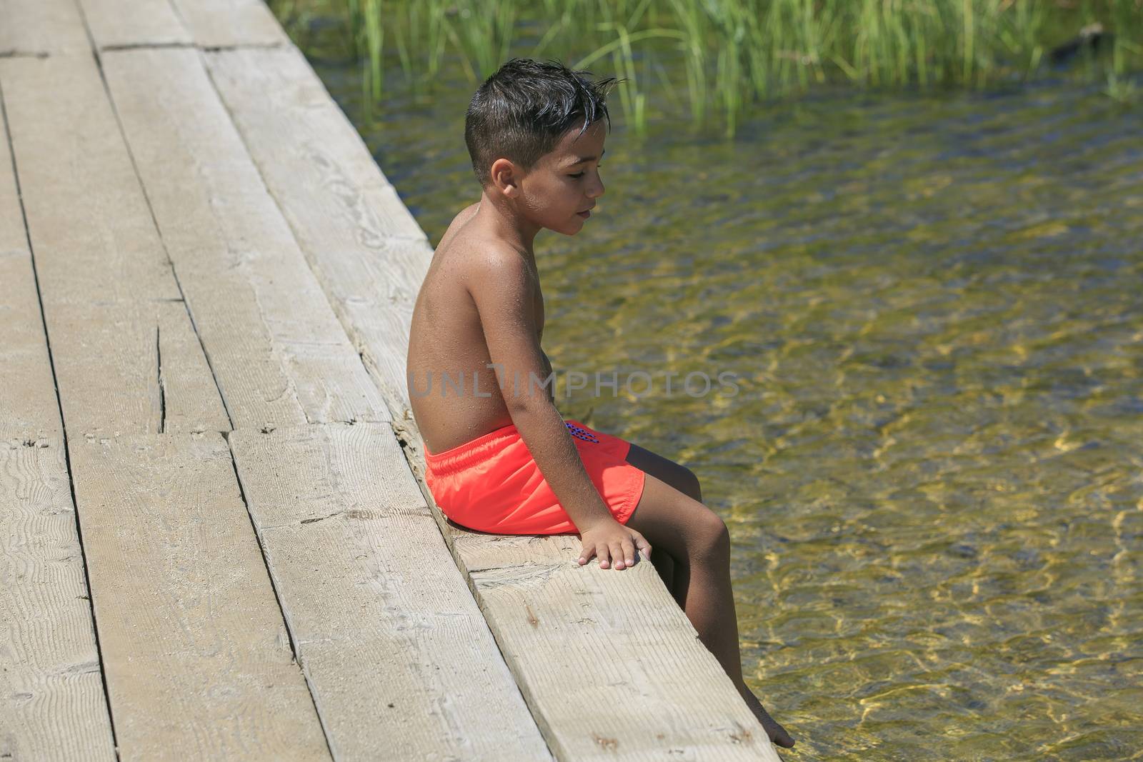 Boy seating on a wooden foot bridge on a lake