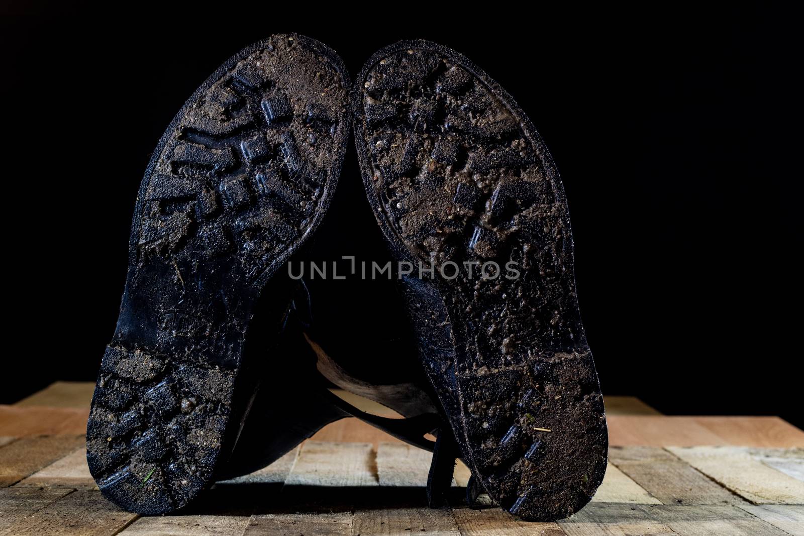 Muddy old military boots. Black color, dirty soles. Wooden table. Black background