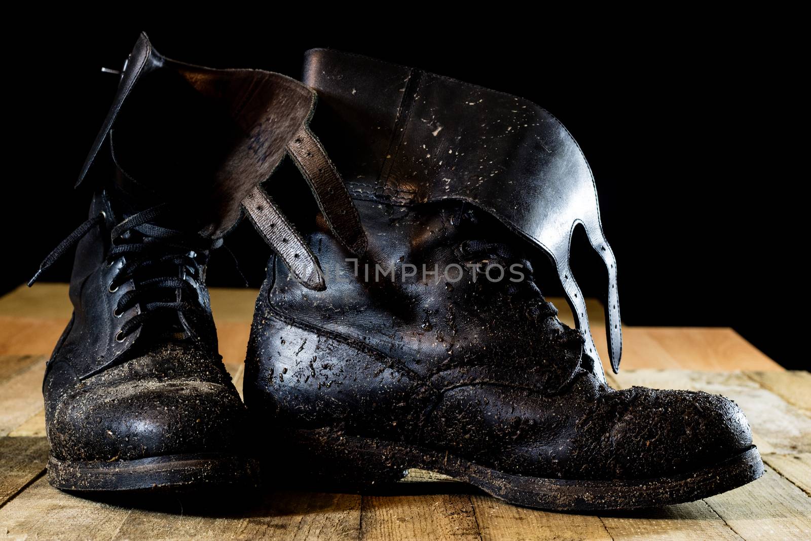 Muddy old military boots. Black color, dirty soles. Wooden table. Black background