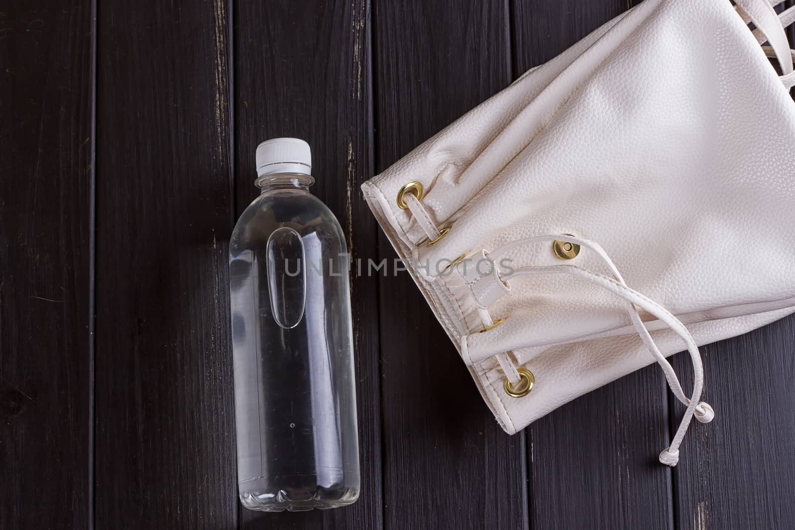 White leather backpack and water bottle on a black wooden background