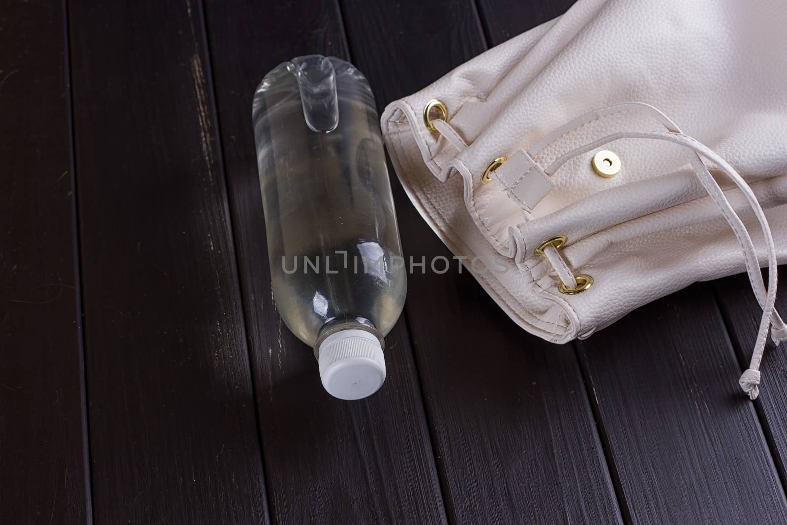 White leather backpack and water bottle on a black wooden background