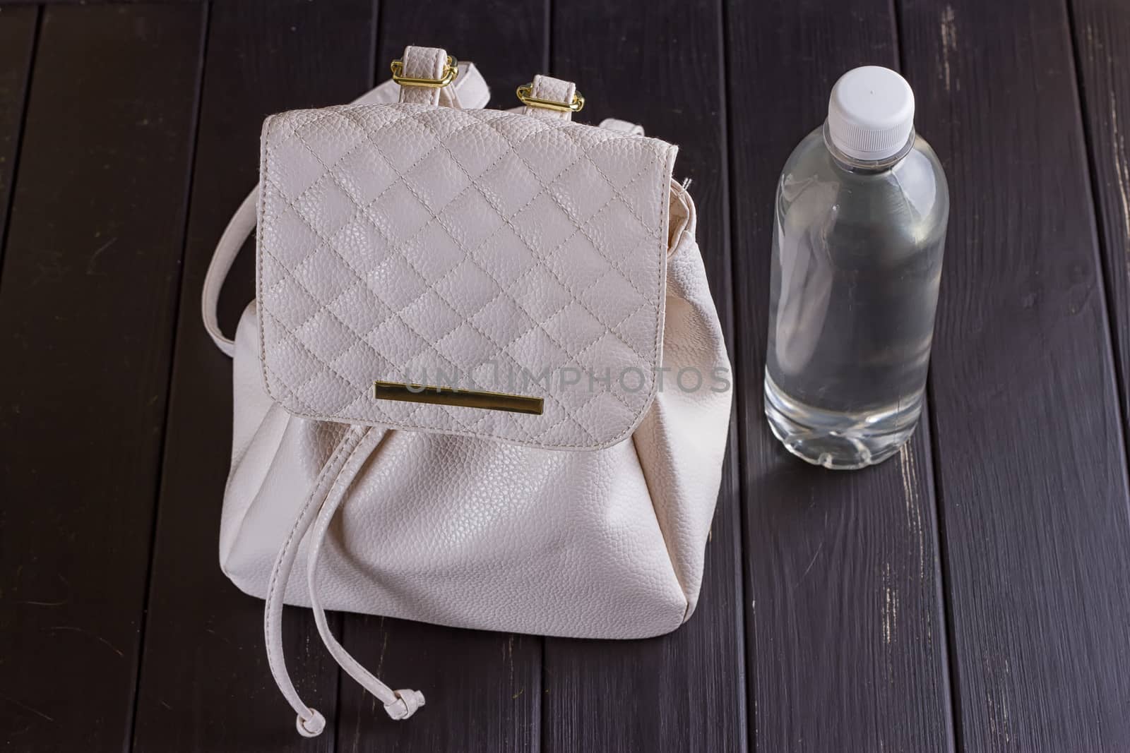 White leather backpack and water bottle on a black wooden background