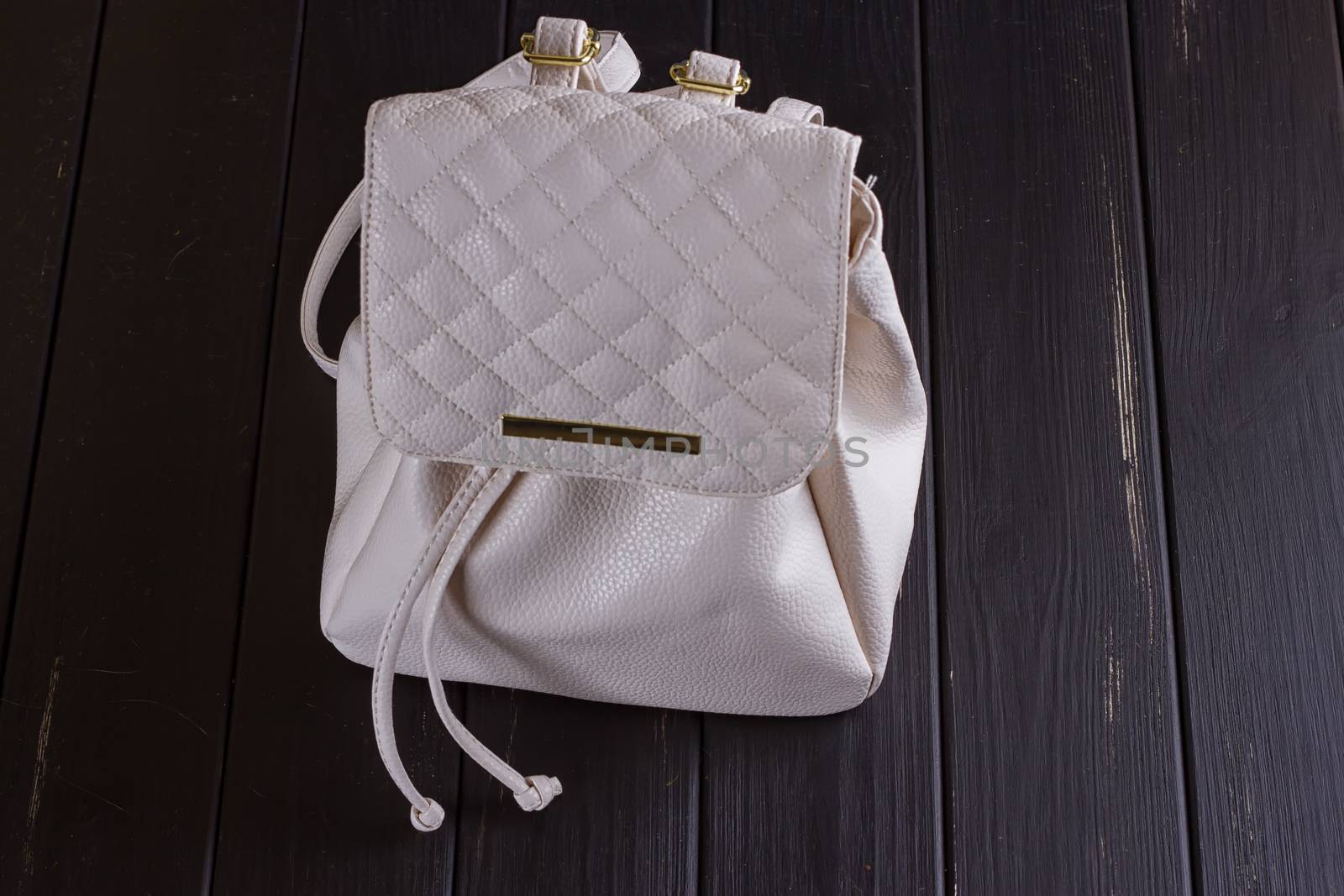 Small white leather female backpack on a black wooden background