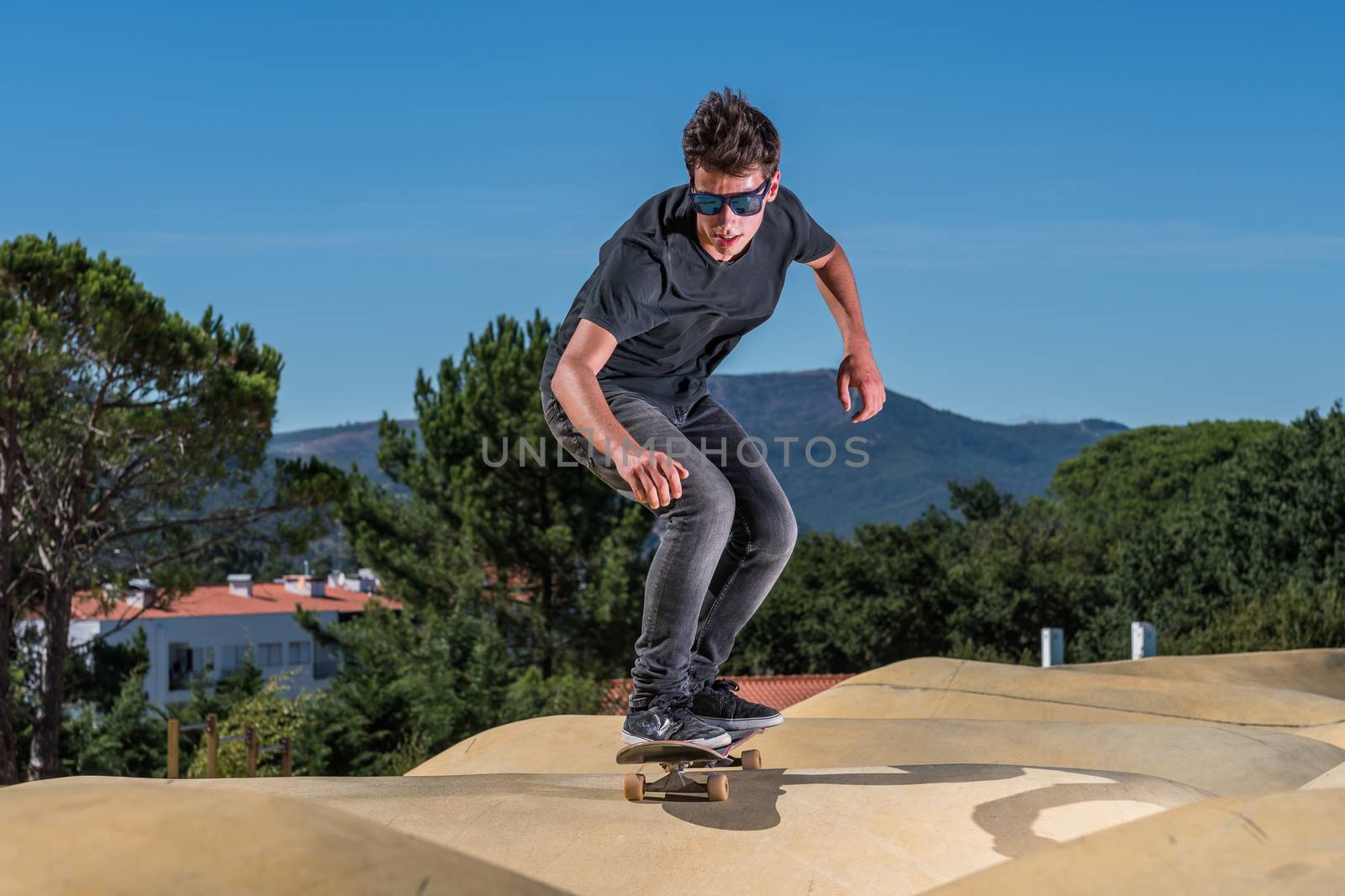 Skateboarder practice on a pump track park on a sunny summer day.
