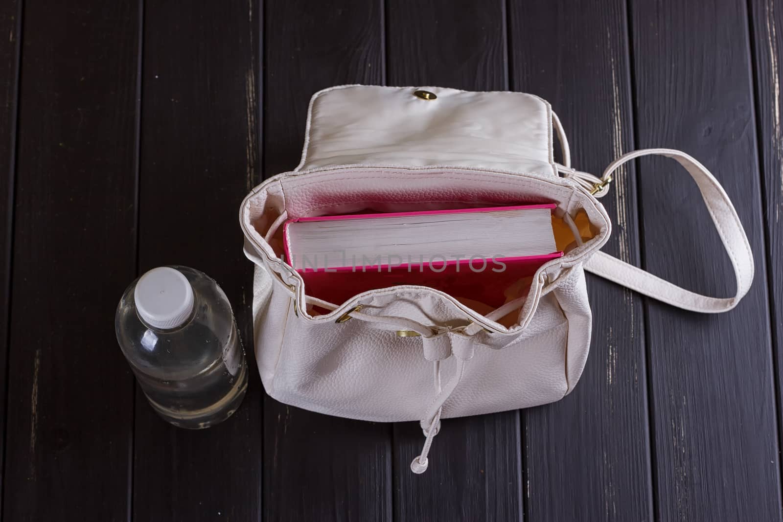 White leather backpack, pink book, bottle of water on a black background