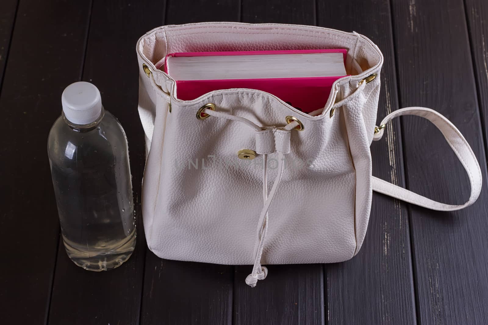 White leather backpack, pink book, bottle of water on a black background