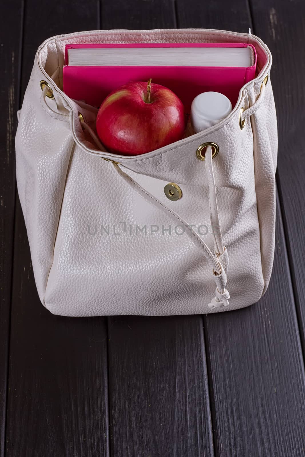 White leather backpack, pink book, bottle of water on a black background