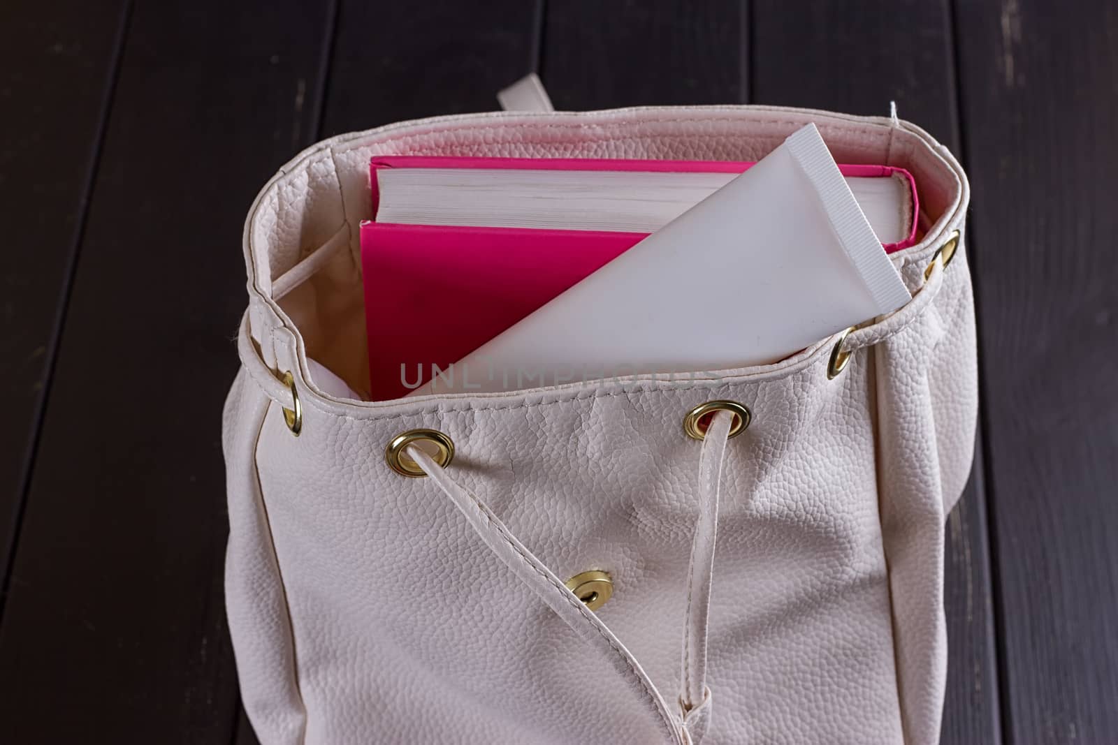 White leather backpack, apple, tube of cream on a black background